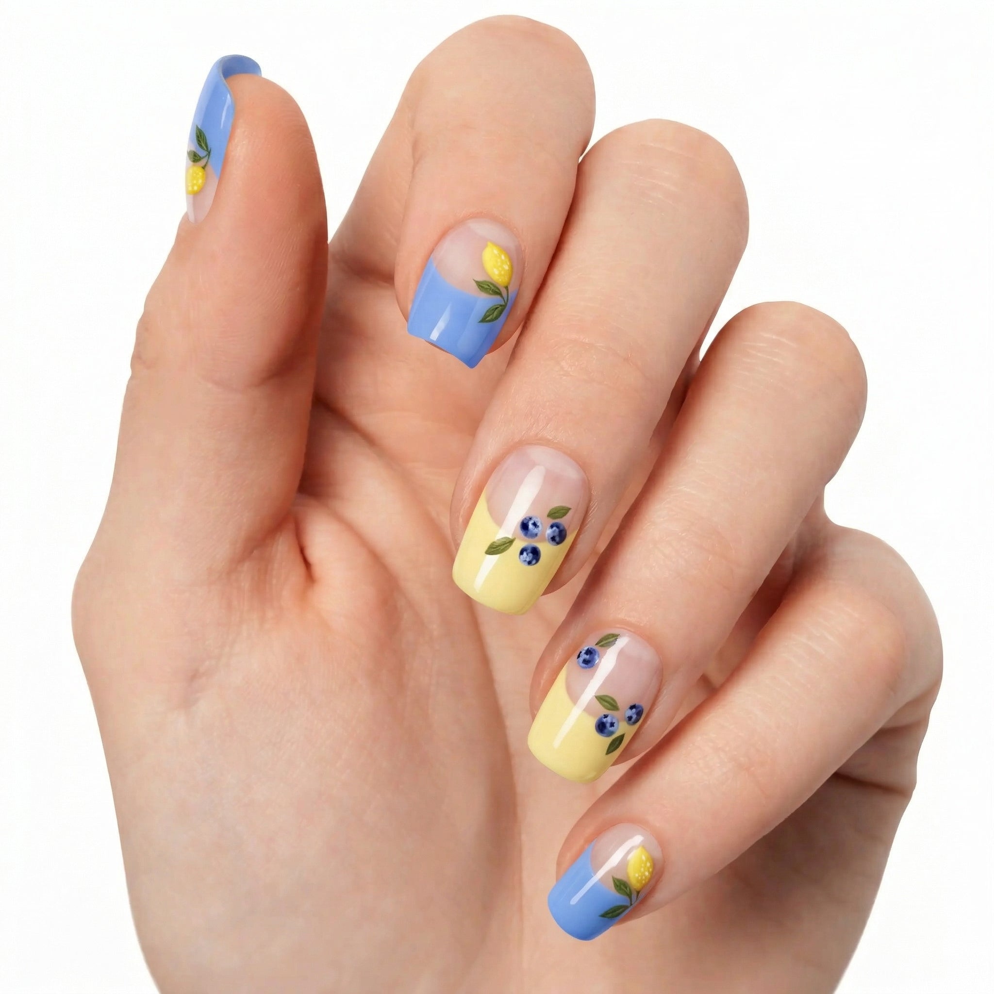 Ongles pastel Glamisu bleu et jaune citron avec motifs fleurs et fruits sur main claire, manucure fraîche et estivale sans UV