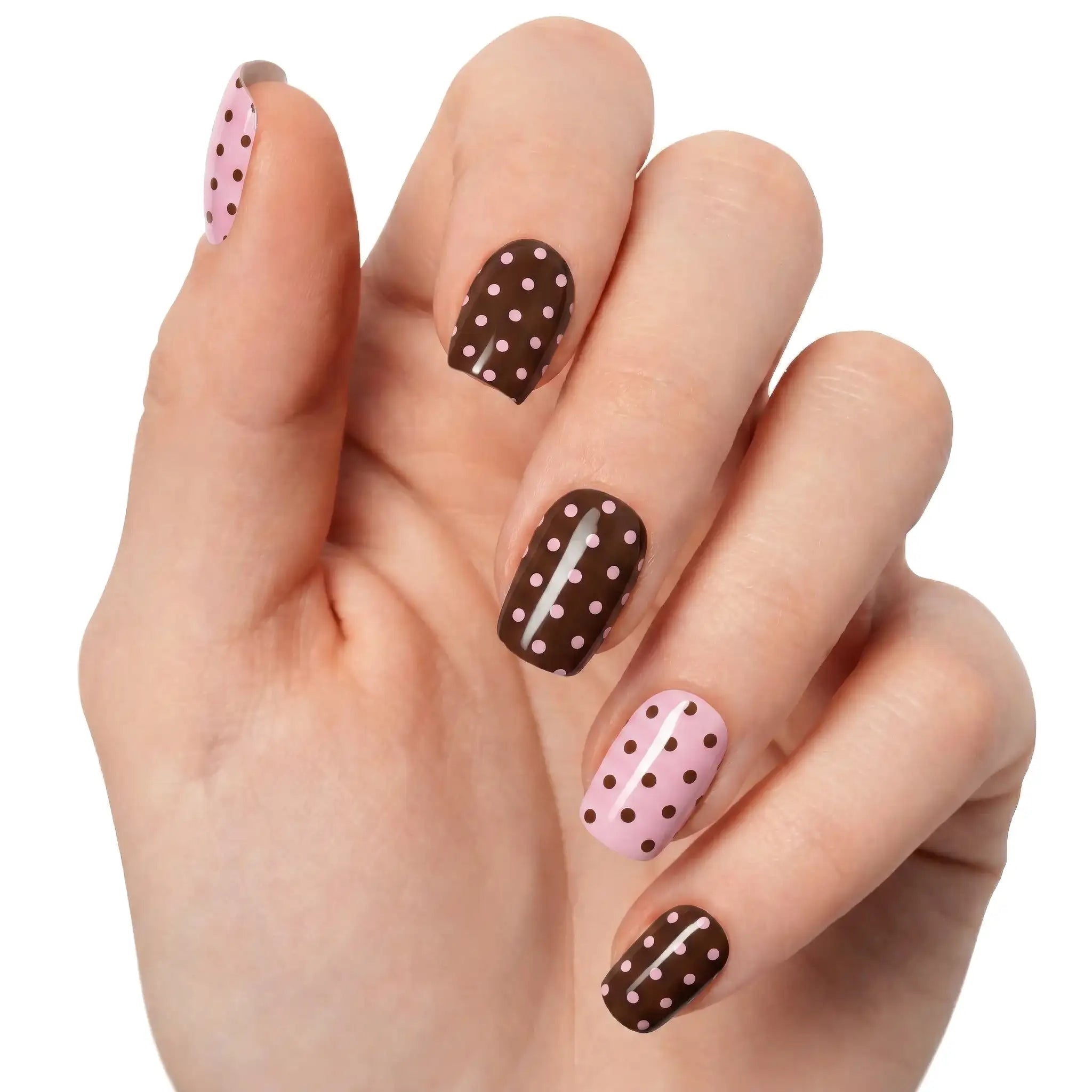 Gros plan sur une main claire avec gel wraps Pois Chocolat N°332, nail art rose et chocolat à pois brillants sur fond clair.